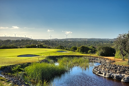 Water hazard guards the green with solar windmills above